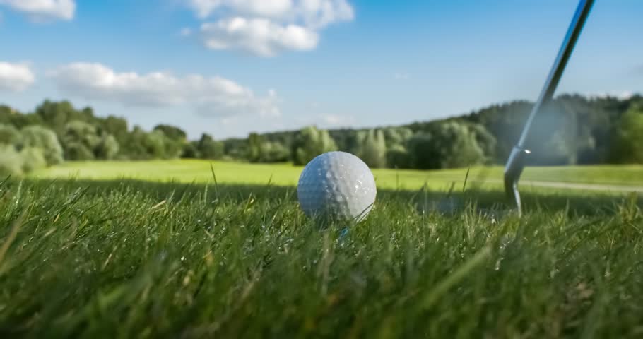 Golf club hits a golf ball in a super slow motion. Drops of morning dew and grass particles rise into the air after the impact.