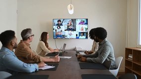 A team actively engages with remote colleagues via a large screen, illustrating the modern hybrid work model where technology bridges the gap between in-office and remote team members - Powered by Shutterstock - Get 15% off with code: PIKWIZARD15