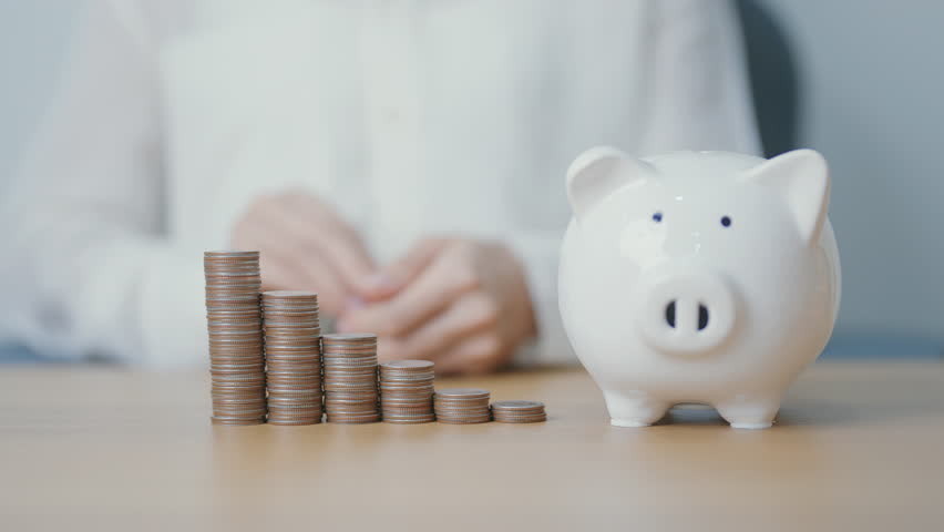 Money Saving for Future Plan, Retirement fund, Pension, Investment, Wealth Business and Financial concepts. hand putting coin into piggy bank on table, Money Counting and stack arrangement for deposit