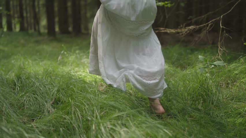 Motion video of legs of a pretty woman running barefooted in forest during daytime. Dense foliage.
