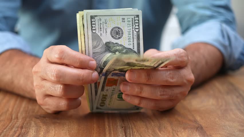 CEO counts dollar banknotes in office calculating cash flow needed to fund next phase of software company innovative project development and expansion