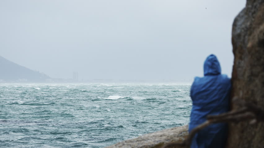 Man in raincoat standing back to camera looking at sea on the pier during the rain. Concept of travel, lonelyness, mood, solitude. South Africa landscape. Heavy rain, bad weather. Copy space