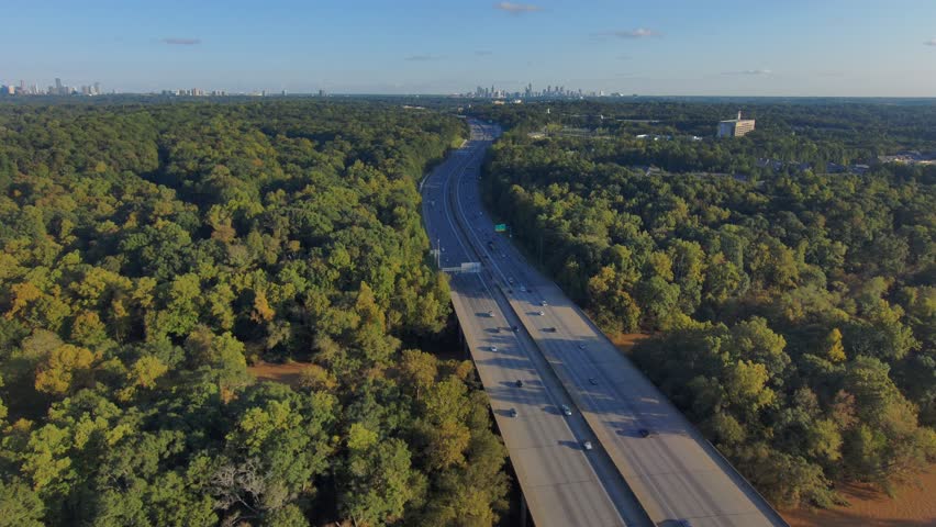 a stunning aerial shot of the lush green and autumn colored trees and the smooth brown waters of the Chattahoochee river with cars driving on the highway with blue sky and clouds in Atlanta Georgia 