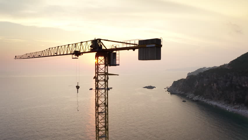 Old rusty industrial Tower crane on the abandoned Perazica Do beach during sunset ligh hours. Petrovac, Adriatic seacoast, Montenegro. 4K flying drone pano video.