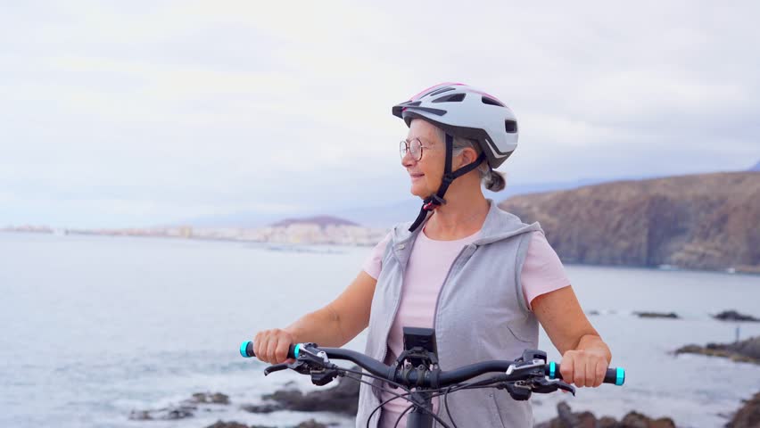 Portrait of one old woman smiling and enjoying nature outdoors riding bike with her husband laughing. Headshot of mature female with glasses feeling healthy. Senior putting on helmet to go trip with b