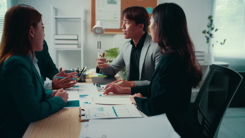 Business team engaging in discussion, sharing ideas and analyzing reports around a conference table in a bright office setting