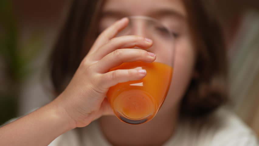 A close-up shot of a little girl drinking freshly squeezed orange juice.