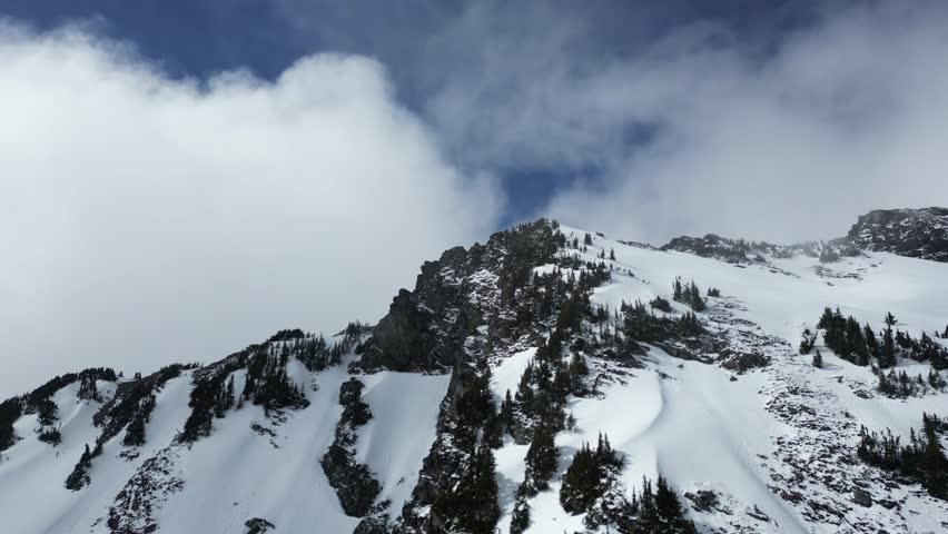 Clouds moving over a snow-capped mountain peak with pine trees. Shot on a bright winter day. British Columbia, Canada