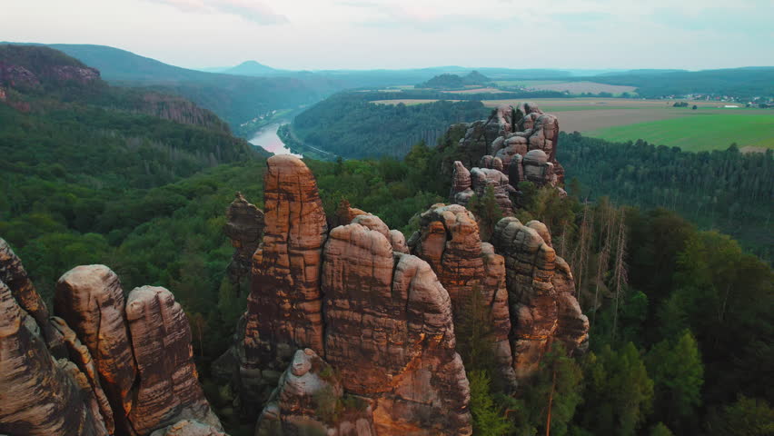 Sunset view of towering rock formations and expansive valleys, dense forests, and a winding river in Saxon Switzerland, Schrammsteine Elbe Sandstone Mountains Germany