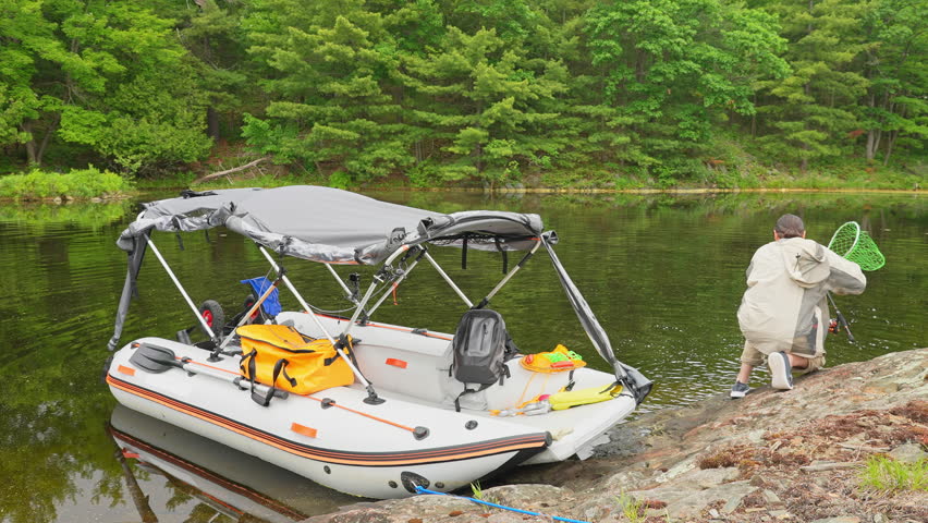 Fisherman sport fishing and net catching Northern pike fish in the lake. Fishing pike on spinning rod and reel. Angler net pulling young pike from water on rocky island. Trophy catch and recreation.