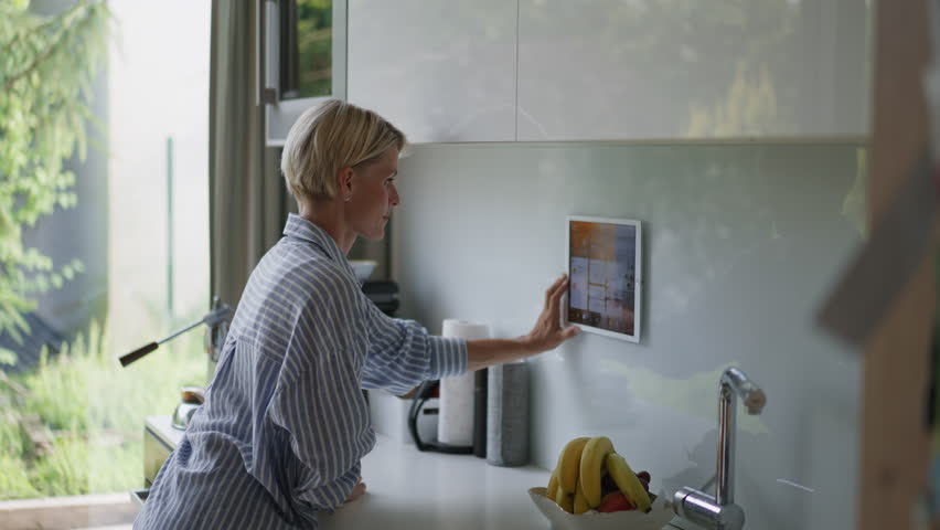 Beautiful woman adjusting smart home settings on touch screen device. Smart home technology for sustainable living.