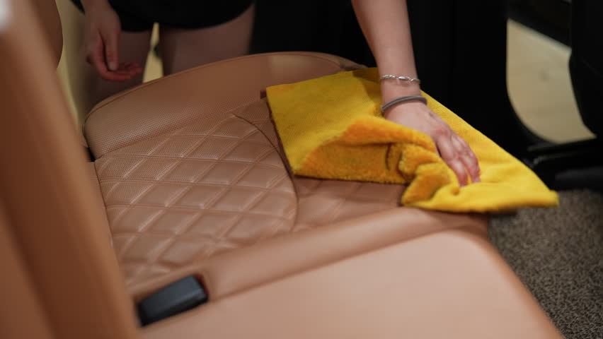 Car detailer meticulously cleaning luxurious leather seat with yellow cloth, showcasing the intricate stitch pattern and glossy sheen. Concept of stages process professional car washing detailing.