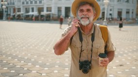 A smiling retired tourist walks through the city on his trip carrying a coffee and talking on the phone. - Powered by Shutterstock - Get 15% off with code: PIKWIZARD15