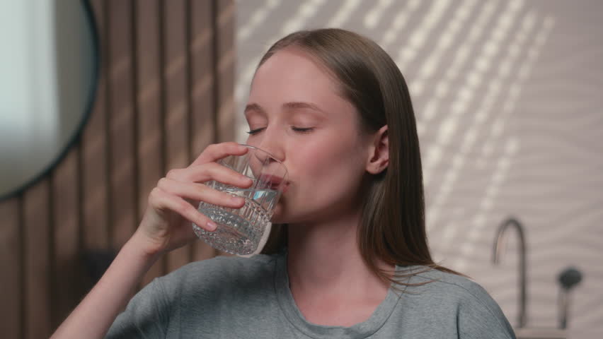Healthy woman Caucasian happy female girl in home bathroom smile drink glass water thirst body care look camera drinking refresh moisturize skin hydration balance beauty skincare health diet vitamins