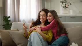 Happy family spending weekend together. Caucasian woman female mother using mobile cell phone online app active little girl child kid schoolgirl daughter jumping on sofa hugging mom inside living room - Powered by Shutterstock - Get 15% off with code: PIKWIZARD15