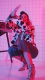Vertical shot of expressive girl in animal print jacket performing dynamic hand moves and duck walk while dancing vogue in studio with colorful neon light, retro boombox and tiled wall - Powered by Shutterstock - Get 15% off with code: PIKWIZARD15