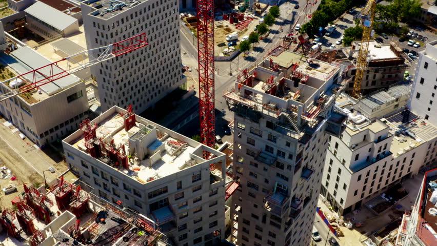 Tower cranes and workers at high concrete residential building under construction. Real estate development concept. Modern crane works with building on a site.