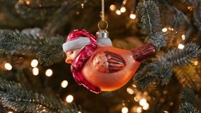 Christmas tree ornament close-up in shape of bird wearing red Santa hat, scarf. Background is decorated with pine branches warm lights creating cozy festive atmosphere. Family holidays. Noel. New year - Powered by Shutterstock - Get 15% off with code: PIKWIZARD15