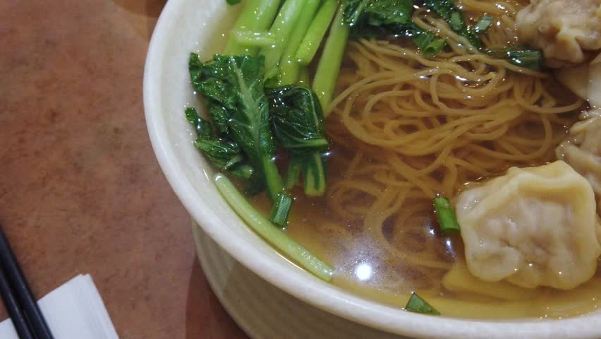 Chinese Wonton (Dumplings) and Egg Noodle Soup (Cantonese style), with some fresh green vegetables as garnish. Catering concept. 4k60.