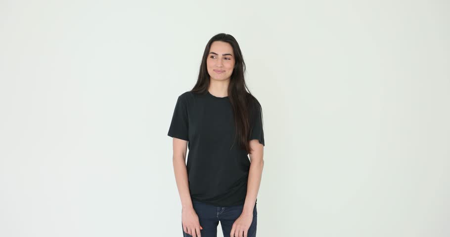 Young woman with long loose dark hair smiles and touching her chin on white background. Female model wearing black t-shirt and jeans