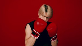 A young athlete dons red boxing gloves while adopting a determined stance against a striking red background. His focused expression indicates readiness for an upcoming match. - Powered by Shutterstock - Get 15% off with code: PIKWIZARD15