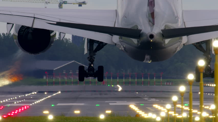 Slow motion footage of an airplane touching down on the runway with its landing gear deployed and the runway lights illuminated during descent