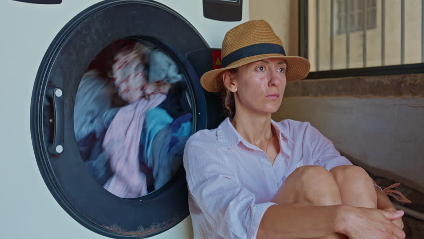 A female tourist in a hat, sitting in a laundry room, waiting for the laundry to finish washing