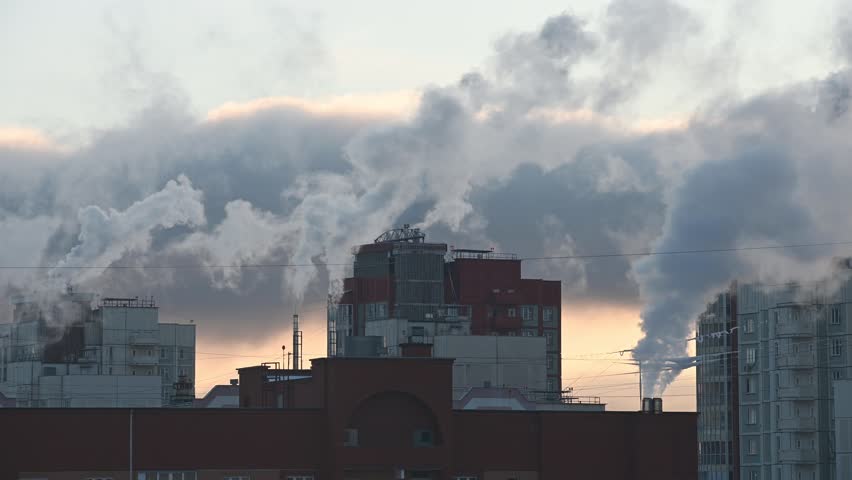 Smoke billows from chimneys atop apartment buildings as the sun rises on a chilly morning, creating a serene urban scene. Central heating concept in winter