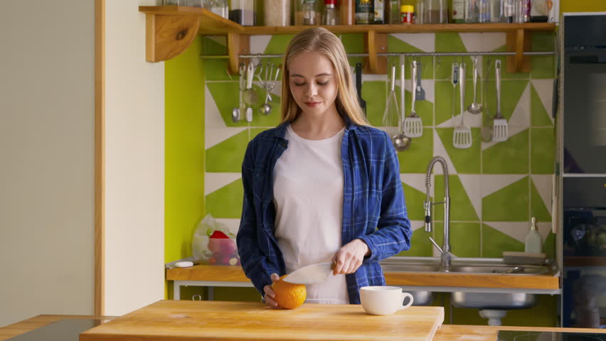A young woman slices an orange in a contemporary kitchen while preparing for breakfast.