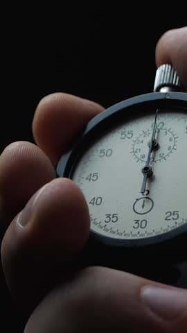 Black analogue stopwatch in hand on black background. Time start with old chronometer. Man presses start button. Sports or business concept, successful teamwork and counting down time