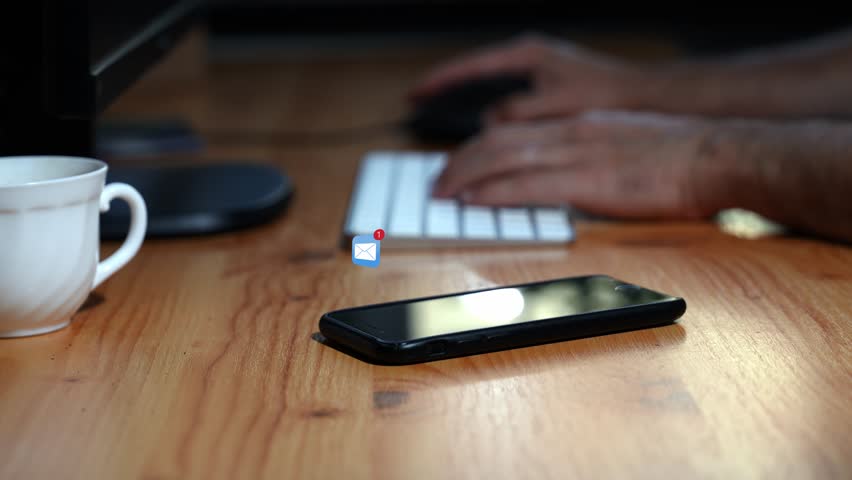 Close-up of a smartphone on a keyboard with a man typing. An email icon appears above the phone, he picks it up, replies, and places it back.