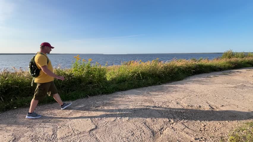 tourist walks with a backpack along the sea, admiring nature. The male persona is enjoying a summer day.