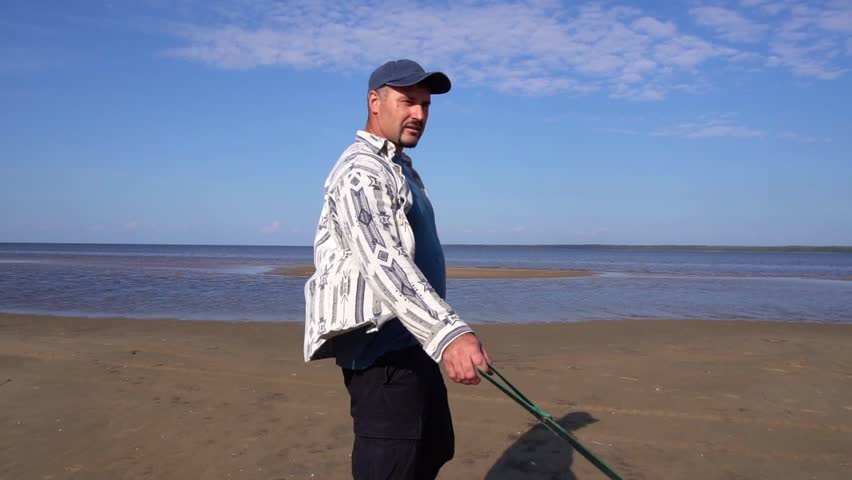 mature 45-year-old Caucasian man walks with a Siberian husky on a leash along the coast of a wide river. summer time.