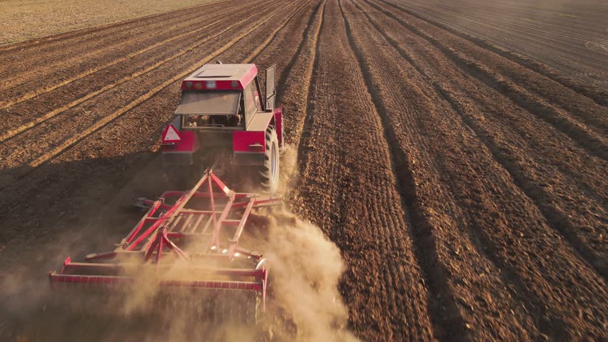 Red tractor working in agricultural field, cultivating and plowing dry soil, aerial view. Agribusiness concept. Small farming concept