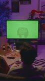 Full vertical rear shot of young students sitting together on couch pizza and beer, watching TV show, sports match or movie, chatting and pointing at green chromakey screen. Template, copy space - Powered by Shutterstock - Get 15% off with code: PIKWIZARD15