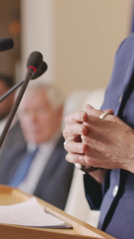 Medium vertical shot of hands of unrecognizable mature female politician standing on tribune, gesticulating during public speech at international conference or election rally