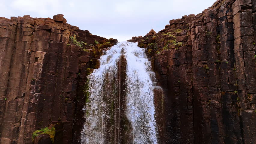 Waterfall in the basaltic cliff. Beautiful rock with the column structure in Iceland. Drone footage.