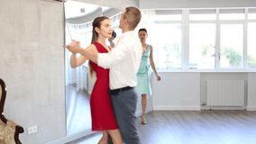 In spacious choreography studio, positive young adult man practicing elegant Viennese waltz with slender brunette in silk aquamarine dress during dance class. High quality 4k footage - Powered by Shutterstock - Get 15% off with code: PIKWIZARD15