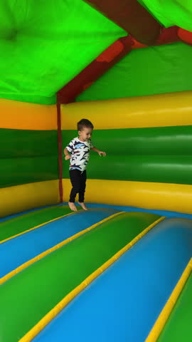 Energetic baby boy runs, falls and tumbles cheerfully inside the inflatable playhouse. Happy active fun time spending. Vertical video.