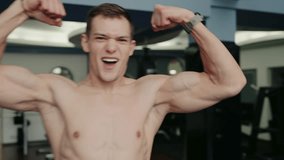A muscled young man in a gym showcasing his biceps with a cheerful expression, promoting fitness and wellbeing. Athletic Young Man Flexing Muscles Confidently in Gym Setting - Powered by Shutterstock - Get 15% off with code: PIKWIZARD15