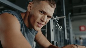 A young man, wearing a sleeveless shirt, intensely focused while working out at a gym. Capturing the essence of determination and fitness. Focused Man Working Out at Gym in Sleeveless Shirt - Powered by Shutterstock - Get 15% off with code: PIKWIZARD15