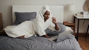 Long shot of young black woman in white bathrobe using wireless laptop when resting in bed with applied under eyes patches - Powered by Shutterstock - Get 15% off with code: PIKWIZARD15