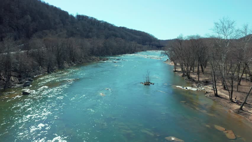 Aerial dolly of a river cutting through a mountainous landscape, with sparkling waters and leaveless trees lining the riverbanks