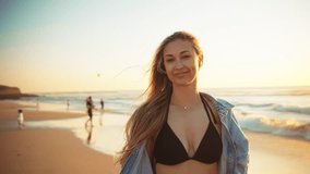 Beautiful woman with long blonde hair in denim shirt stands by ocean playfully enjoying sunset rays. Scene captures serene moment during her travels by the sea - Powered by Shutterstock - Get 15% off with code: PIKWIZARD15