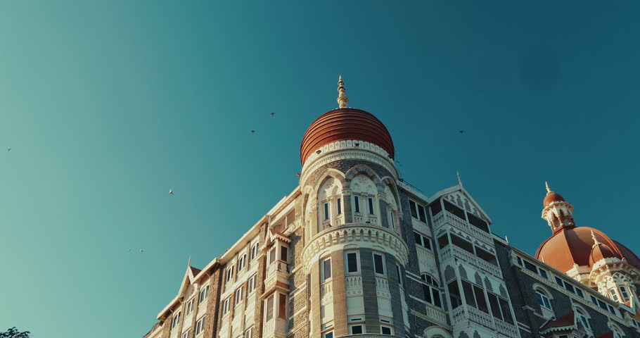 Mumbai, India. Pigeons Fly In Slow Motion Above Taj Mahal Hotel. Black Kite Sit On Taj Mahal Palace. Five-star, Luxury Hotel, Situated Next To Gateway Of India. Slow Motion Birds Fly Above Taj Mahal