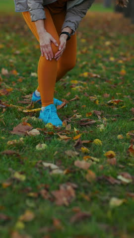 Hello autumn. Closeup on woman in fitness clothes in the park with knee pain.