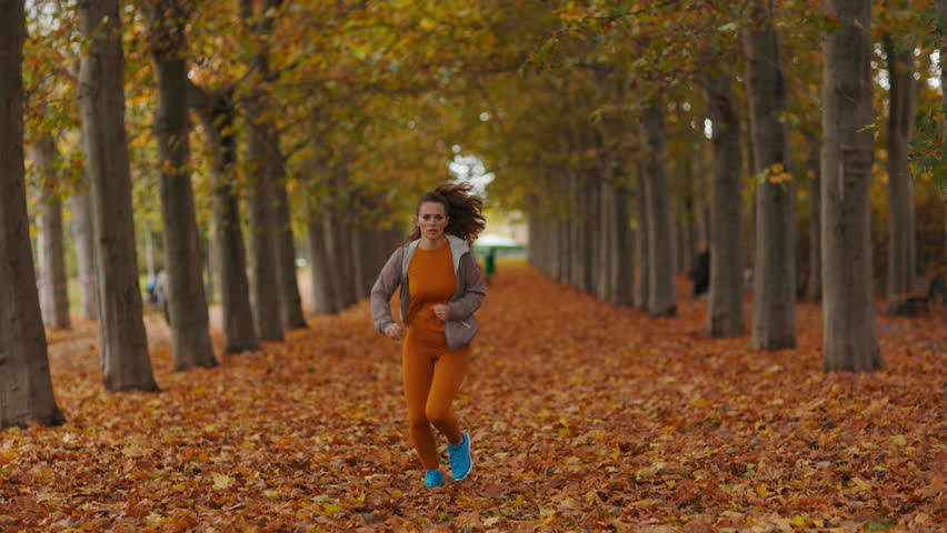Hello autumn. happy trendy 40 years old woman in fitness clothes in the park running.