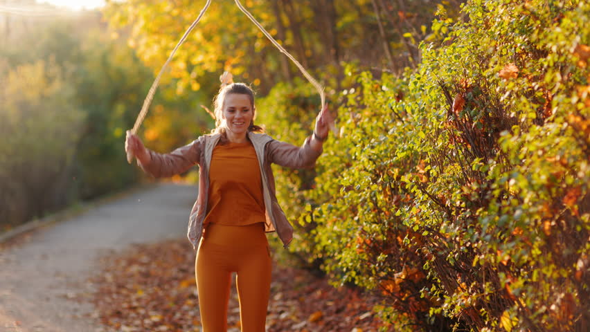 Hello autumn. fit 40 years old woman in fitness clothes in the park with jump rope training.
