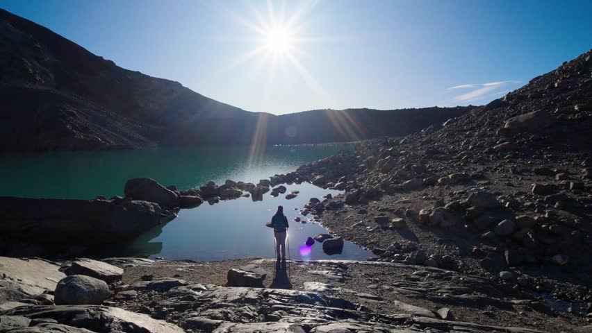 Lonelyhiker woman stood and watched mountain lake. Free tourist woman looking at sun enjoying landscape. Girl traveler with backpack stands on top of mountain in rays of sunset. hiker is enjoying natu