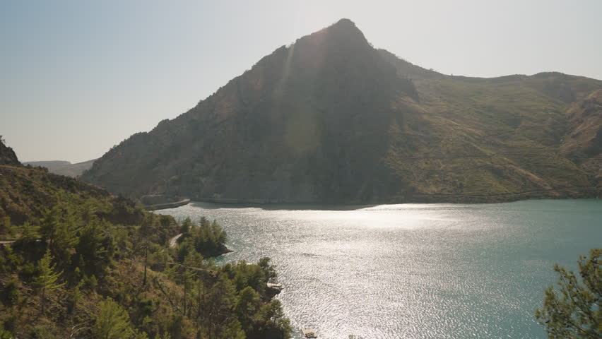 Sunlight Reflects Off Turquoise Lake as Camera Pans Across Majestic Mountain, Capturing the Serene Beauty and Expansive Landscape in Slow Motion.